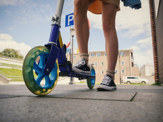 Legs of young woman on kick scooter at street.