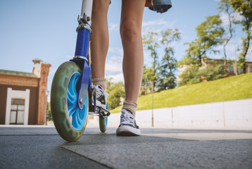 Naklejka premium Legs of young woman on kick scooter at street.