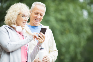 Aged female showing her husband something in smartphone after outdoor workout