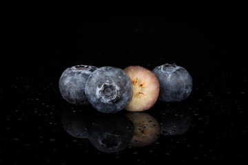 Group of Blueberries, one cut in half isolated on a reflective surface, water droplets, close up