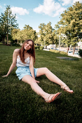 Pretty young girl sitting next to bike in grass and having a rest