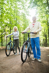 Obraz premium Retired couple in activewear standing on road in park by their bicycles