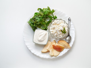 Cottage cheese and sour cream in glass plates lies on a white plate with cilantro greens and slices of fresh apple