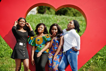 Group of four african american girls against big red heart outdoor sending air kisses.