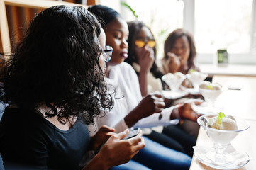 Four african american girls sitting on table at cafe and eating ice cream dessert.