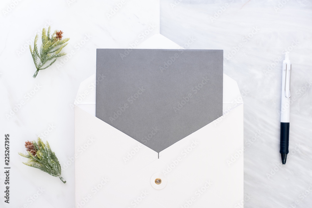 Poster Top view of blank grey card in white envelop with pen and pine leaf on two layer step of marble table top.Mock up template for display of design.modern business items.