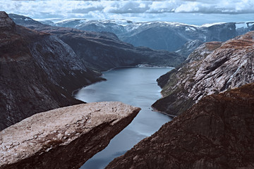 Tourist man sitting in the Trolltunga and enjoys the beautiful view of the Norwegian fjord.