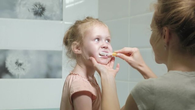 Mom gently brushes the teeth of her beloved daughter A little girl with her mother gently cleans teeth after eating.