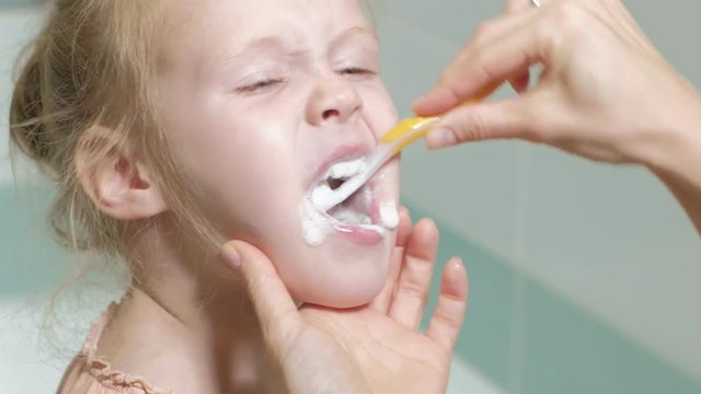Mom gently brushes the teeth of her beloved daughter A little girl with her mother gently cleans teeth after eating.
