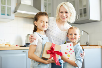 Young cheerful female embracing her two daughters with gifts for mom day