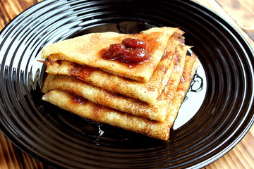 thin pancakes stacked on a plate and poured with jam