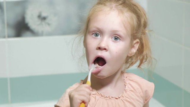 Little girl diligently brushing his teeth in the mirror.