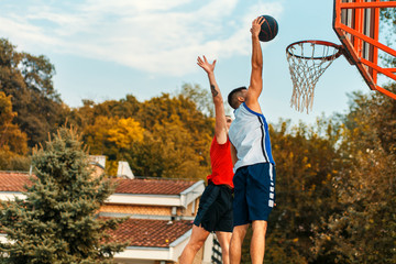 Two young friends playing basketball on court outdoors during the day.