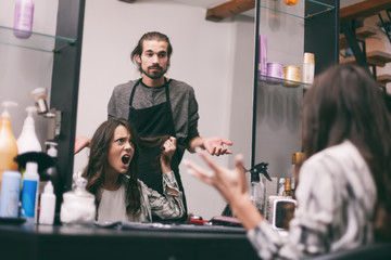 Young woman getting new hairstyle at professional hair styling saloon. She is not satisfied with her new hairstyle. © djoronimo