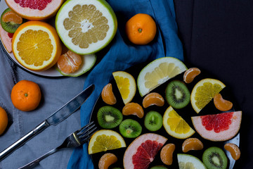 many citrus fruits are sliced in two plates black and white, half grapefruit orange sweeties big and little blue grey black rags towel dark