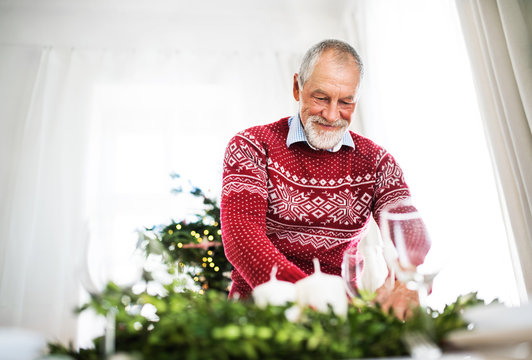 A senior man setting a table for a dinner at home at Christmas time.