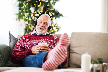 A senior man with headphones listening to music at home at Christmas time.