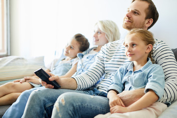 Young family of parents and two little daughters sitting on sofa and watching tv