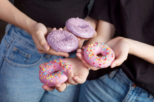 Close up donuts in girls hands. Two girls holding fresh colorful donats