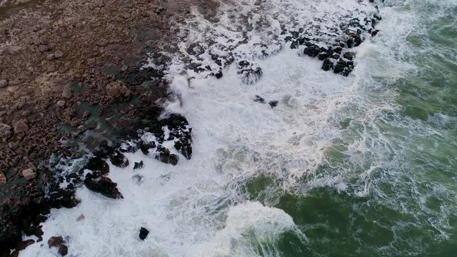  Aerial view of rocky coastline with crashing waves.