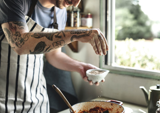 Tattooed man cooking in rustic kitchen