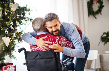 A hipster man hugging his senior father in wheelchair at Christmas time.