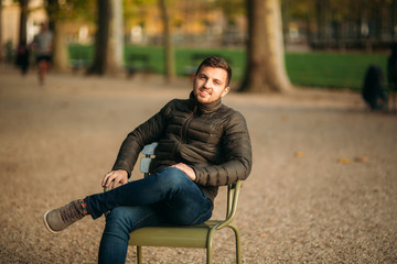 Obraz premium Handsome man sits in the middle of the park in khaki stool