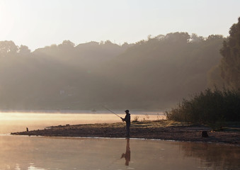 Morning landscape of the river in the light of a rising sun with the fisherman's silhouette