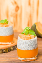 Chia pudding with pumpkin puree in beautiful glasses with green mint leaves and fresh ripe vegetable.