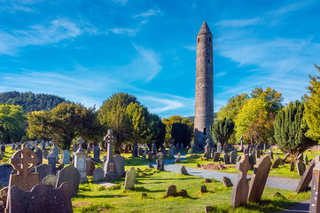Obraz premium Kamienna okrągła wieża i niektóre ruiny osady klasztornej pierwotnie zbudowanej w VI wieku w dolinie Glendalough, hrabstwo Wicklow, Irlandia