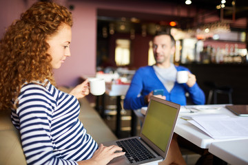 Coworking space for business: serious pensive female entrepreneur with curly hair drinking coffee and browsing internet on laptop