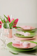Happy easter. Decor and table setting of the Easter table is a vase with pink tulips and dishes of pink and green color.