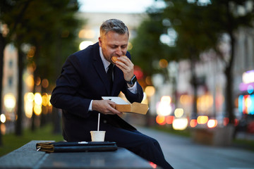 Hungry man in suit eating his sandwich in hurry during short break between parts of business...