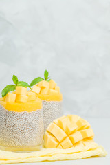 Chia seeds pudding with mango puree in beautiful glasses with green mint leaves and cut fresh ripe tropical fruit.