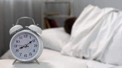 Sleeping man ignoring bed clock in morning, time management, self-discipline