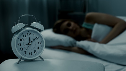 Young lady resting in her bed, midnight time shown on alarm clock, night dreams