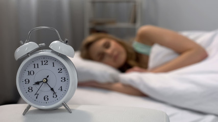 Woman oversleeping in morning, alarm clock ringing near bed, daily routine