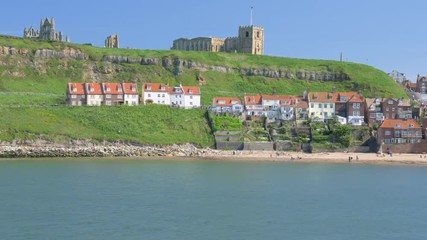 Whitby Abbey and the harbour and beach as evening approaches on a sunny day.