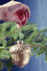 Glass acorn Christmas decoration in hand against green Christmas tree. Holidays Christmas tree decoration 