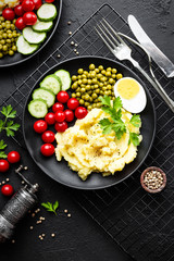 Mashed potato with green peas, tomatoes and boiled egg. Potato puree on plate with vegetables and egg