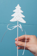 White wooden Christmas decoration in hand against bright color wall. Holidays Christmas tree decoration 