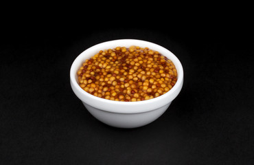 French mustard in white bowl on black background