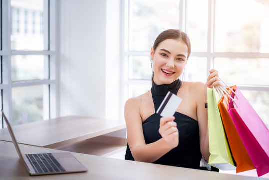 Attractive young businesswoman enjoy shopping online with full of bags with laptop and credit card at office. Have a colorful shopping bags hold on hand. 