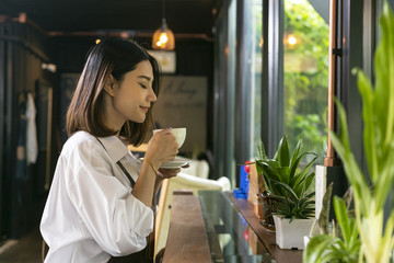 Asian woman smelling and drinking hot coffee with feeling good in cafe.