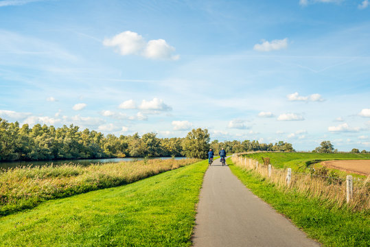 Elderly man and woman cycling on a bike path at the top of a dike at the edge of the Dutch National Park De Biesbosch
