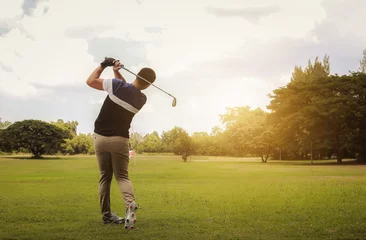 Gordijnen Golfer hitting golf shot with club on course at evening time. © jayzynism