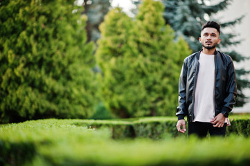 Stylish indian beard man at black leather jacket. India model posed at green garden of city.