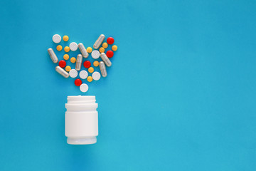 Pills heart out of pill bottle on blue background, top view