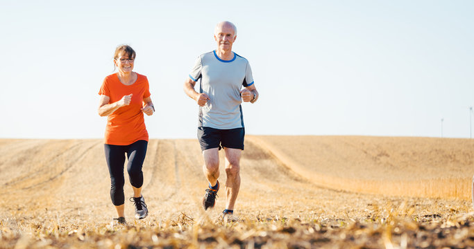 Senior woman and man running or jogging on a field to remain fit and healthy