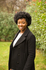 African American woman with curly hair smiling outside.